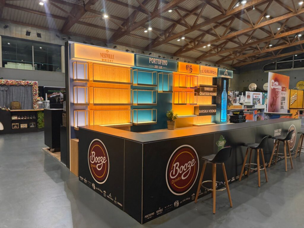 Vista lateral do stand Booze Drinks com bancos altos e prateleiras iluminadas
