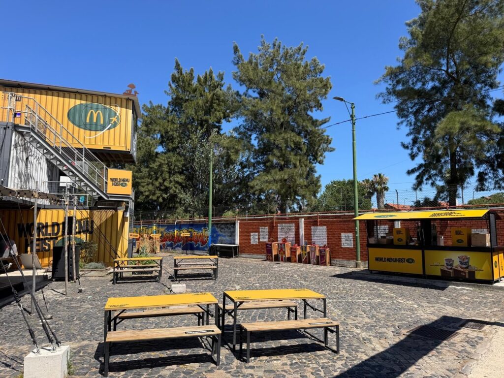 Recinto da ativação World Menu Heist com mesas e contentores